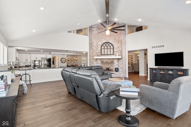 living room with a fireplace, high vaulted ceiling, ceiling fan, light hardwood / wood-style flooring, and beam ceiling