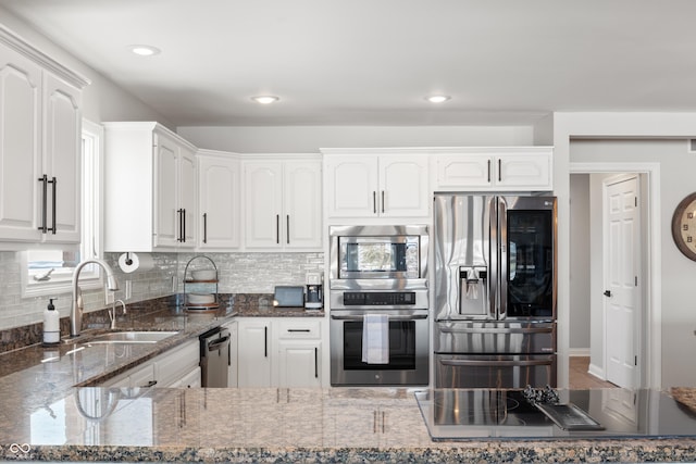 kitchen with stainless steel appliances, backsplash, white cabinetry, a sink, and dark stone countertops