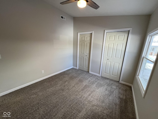 unfurnished bedroom with two closets, vaulted ceiling, ceiling fan, and dark colored carpet