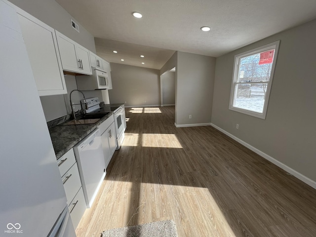 kitchen featuring dark wood-type flooring, sink, white cabinetry, dark stone countertops, and white appliances