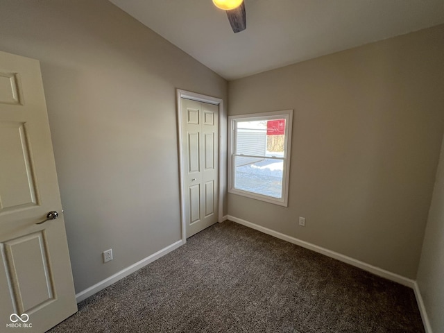 unfurnished bedroom with ceiling fan, lofted ceiling, dark carpet, and a closet