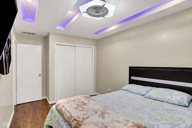 bedroom with a textured ceiling, ceiling fan, a closet, and dark hardwood / wood-style floors