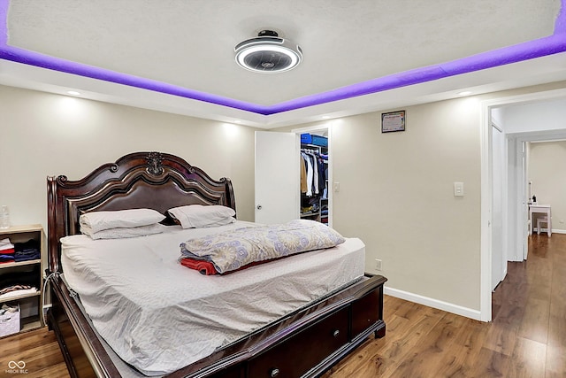 bedroom with a closet, a walk in closet, hardwood / wood-style floors, and a tray ceiling