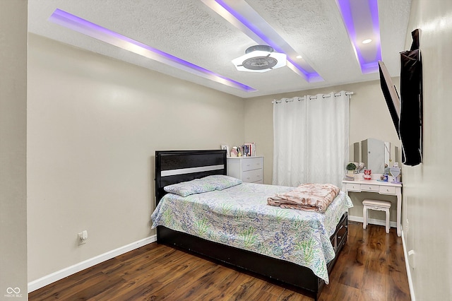 bedroom with ceiling fan, a textured ceiling, a tray ceiling, and dark hardwood / wood-style flooring