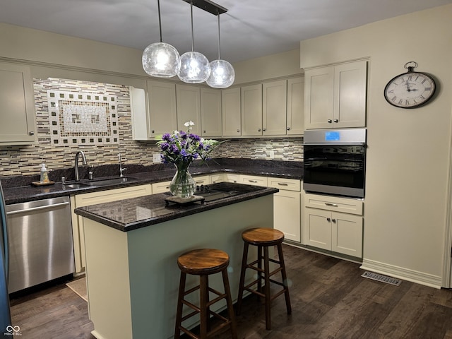 kitchen with sink, appliances with stainless steel finishes, backsplash, a kitchen island, and dark wood-type flooring