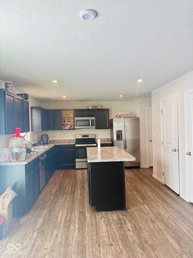 kitchen with stainless steel appliances, blue cabinets, a center island, light hardwood / wood-style flooring, and light stone countertops