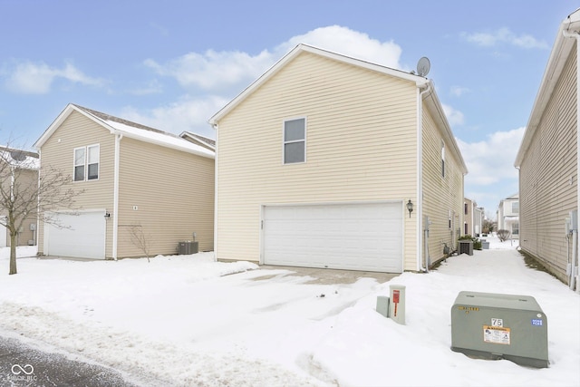 snow covered rear of property featuring central AC and a garage