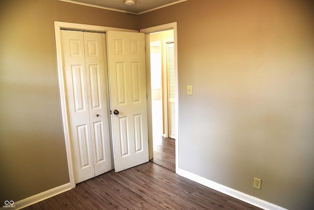 unfurnished bedroom with dark wood-type flooring, a closet, and ornamental molding