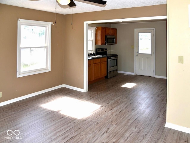 kitchen with ceiling fan, stainless steel appliances, light wood-type flooring, a textured ceiling, and sink