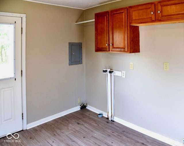 clothes washing area with electric panel, light hardwood / wood-style floors, and cabinets