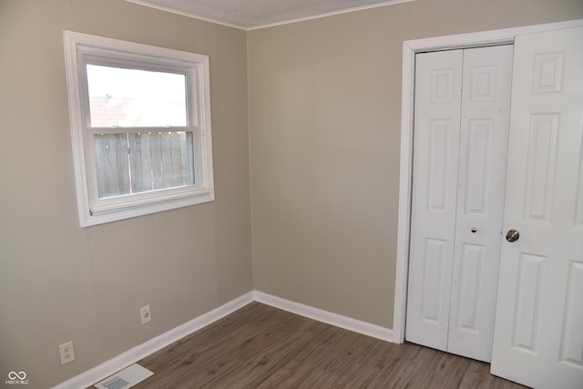 unfurnished bedroom with a closet, dark hardwood / wood-style floors, and ornamental molding