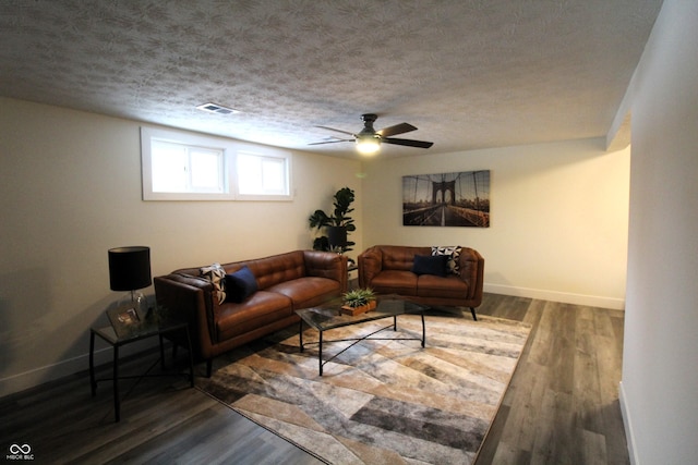 living room featuring dark wood-type flooring, ceiling fan, and a textured ceiling