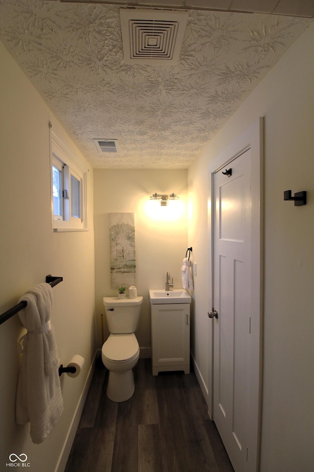 bathroom with wood-type flooring, toilet, vanity, and a textured ceiling