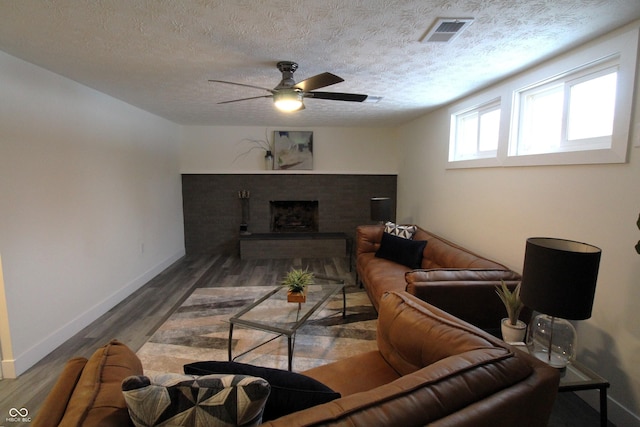 living room featuring ceiling fan, a brick fireplace, dark hardwood / wood-style floors, and a textured ceiling