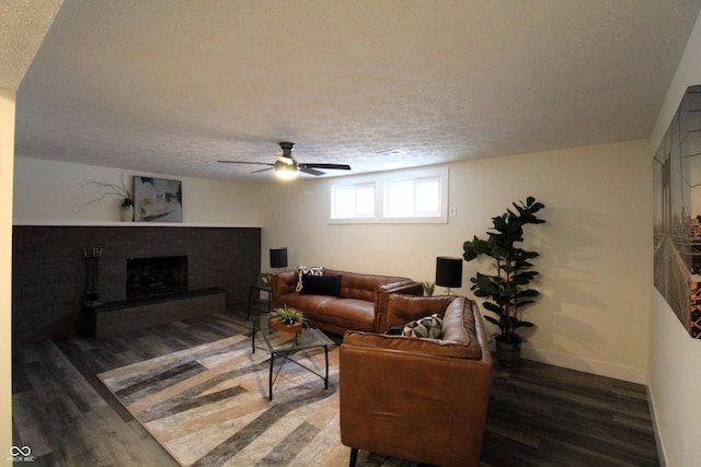 living room with ceiling fan, dark hardwood / wood-style flooring, a brick fireplace, and a textured ceiling