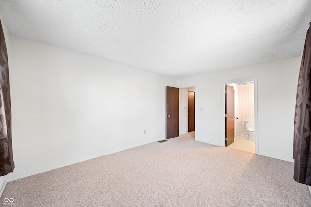 unfurnished bedroom featuring a textured ceiling, light colored carpet, and ensuite bath