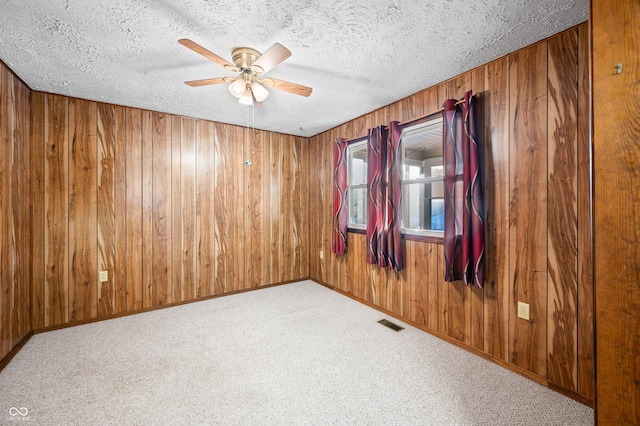 carpeted empty room with ceiling fan, wood walls, and a textured ceiling