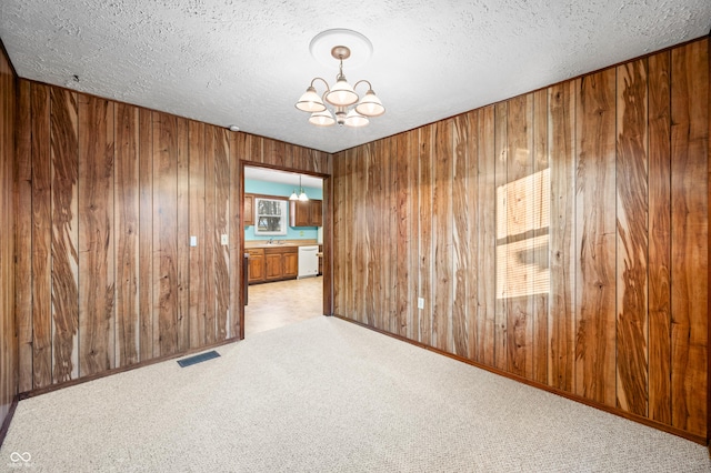 empty room with sink, a textured ceiling, light carpet, and a chandelier