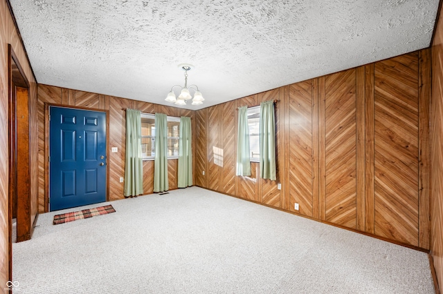 interior space with carpet, wood walls, a chandelier, and a textured ceiling