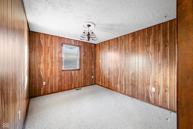 unfurnished room featuring a textured ceiling, light carpet, and a notable chandelier