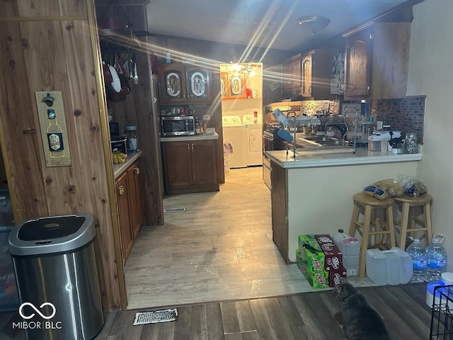 kitchen with a textured ceiling, decorative backsplash, independent washer and dryer, and light hardwood / wood-style flooring