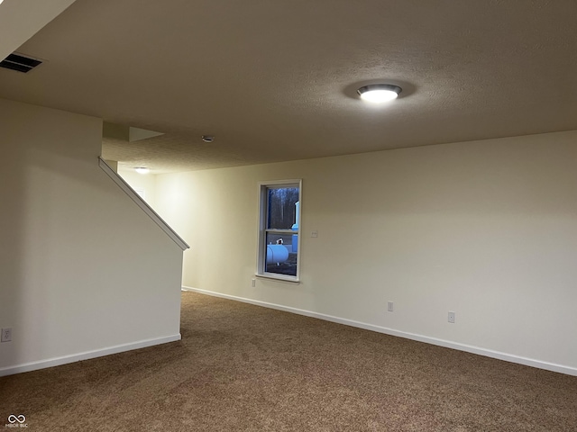 finished basement featuring visible vents, dark carpet, a textured ceiling, and baseboards