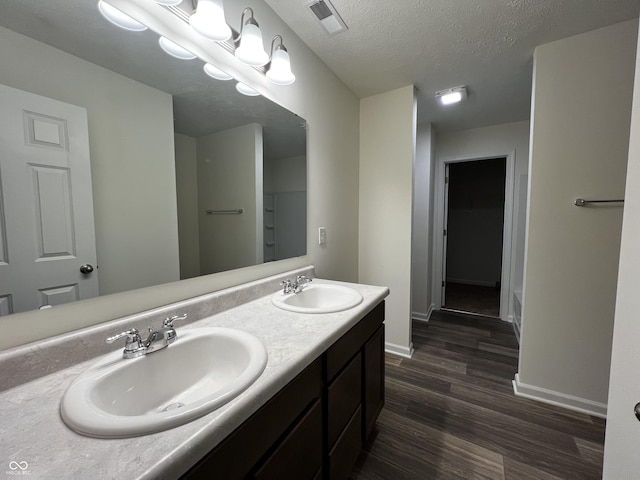 full bathroom featuring a textured ceiling, wood finished floors, a sink, and visible vents