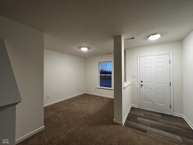 entrance foyer featuring visible vents, dark carpet, a textured ceiling, and baseboards