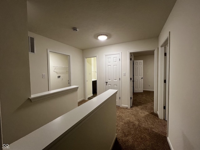 hall featuring a textured ceiling, carpet flooring, visible vents, an upstairs landing, and baseboards