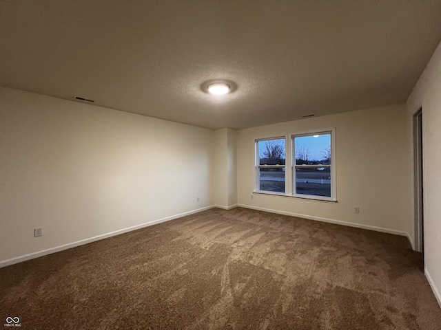 spare room with baseboards, visible vents, dark colored carpet, and a textured ceiling