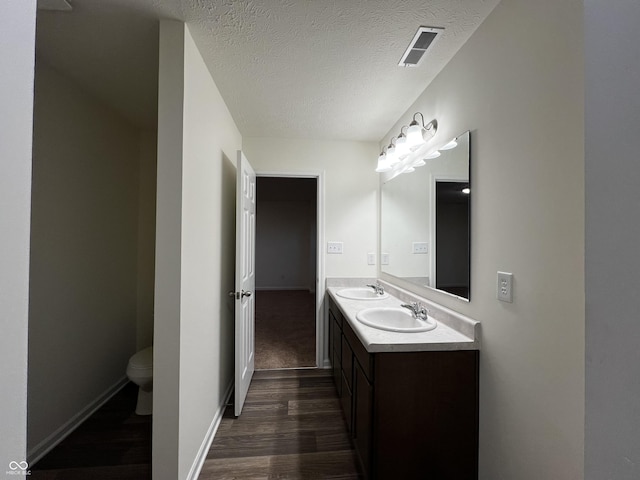 full bath with visible vents, toilet, wood finished floors, a textured ceiling, and a sink