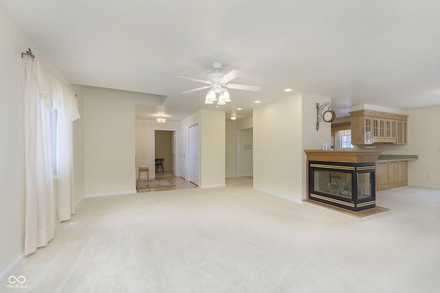 unfurnished living room with ceiling fan, a multi sided fireplace, and light colored carpet