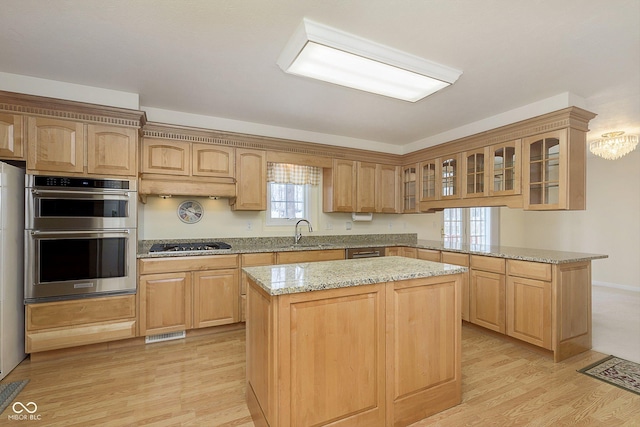 kitchen featuring black gas stovetop, a center island, light stone counters, and stainless steel double oven