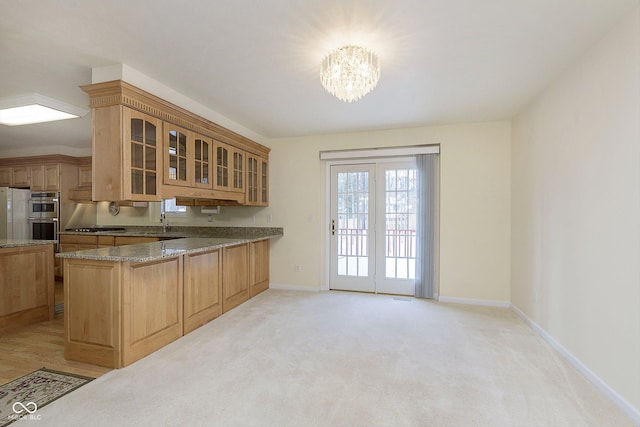 kitchen featuring light stone countertops, stainless steel appliances, an inviting chandelier, kitchen peninsula, and light colored carpet