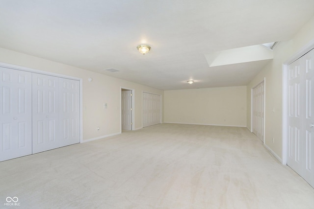 interior space featuring a skylight, two closets, and light colored carpet