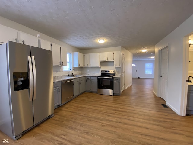 kitchen with stainless steel appliances, gray cabinetry, light wood-type flooring, a textured ceiling, and sink