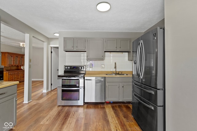 kitchen featuring sink, backsplash, gray cabinetry, and stainless steel appliances