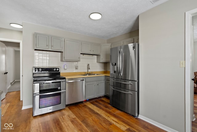 kitchen with gray cabinetry, sink, dark hardwood / wood-style flooring, backsplash, and stainless steel appliances