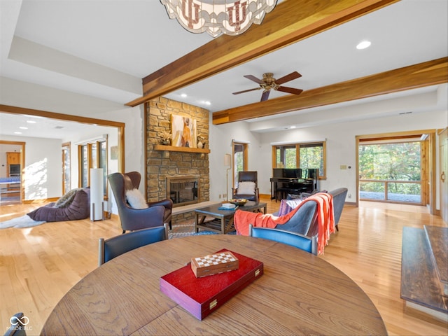 dining area with beam ceiling, a stone fireplace, light hardwood / wood-style flooring, and ceiling fan with notable chandelier