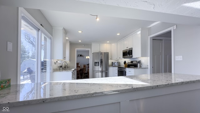 kitchen featuring white cabinetry, stainless steel appliances, light stone counters, tasteful backsplash, and kitchen peninsula