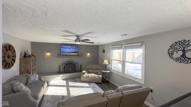 living room featuring a brick fireplace, hardwood / wood-style floors, a textured ceiling, and ceiling fan