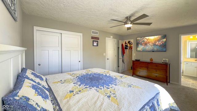 bedroom featuring ensuite bath, ceiling fan, a textured ceiling, light colored carpet, and a closet