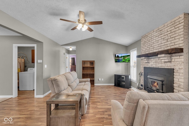 living room featuring ceiling fan, vaulted ceiling, a brick fireplace, washer / clothes dryer, and light wood-type flooring