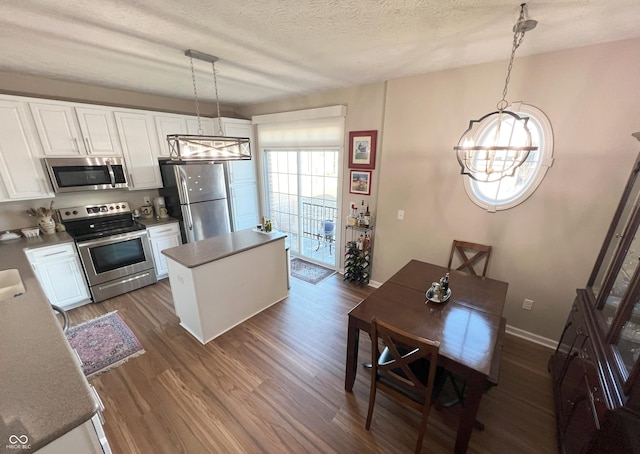 kitchen with white cabinetry, hanging light fixtures, a center island, stainless steel appliances, and a textured ceiling