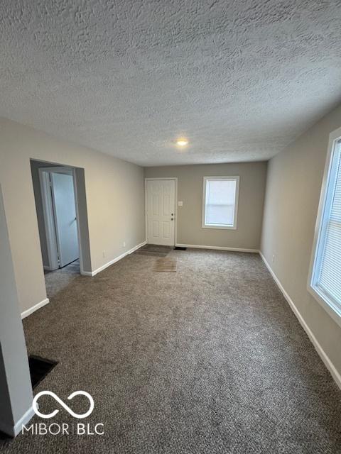 unfurnished room with a textured ceiling and dark colored carpet