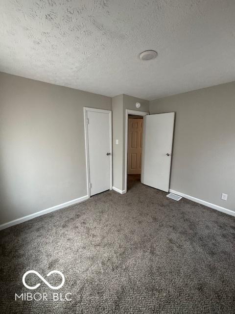 unfurnished bedroom featuring a textured ceiling and dark colored carpet