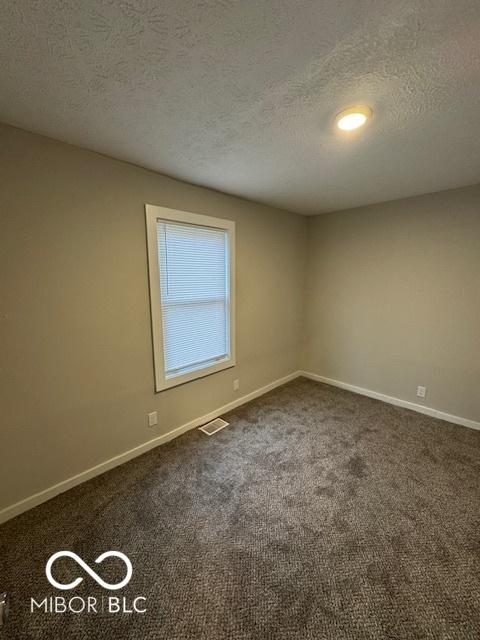 carpeted empty room featuring a textured ceiling