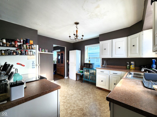 kitchen with a sink, dark countertops, black appliances, and white cabinetry