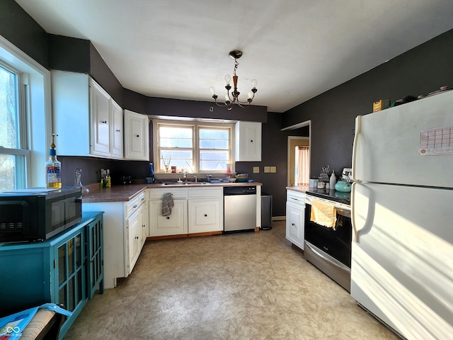 kitchen featuring dark countertops, stainless steel appliances, an inviting chandelier, white cabinetry, and a sink