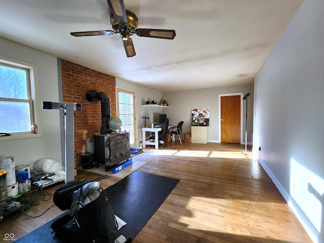 workout area with a wood stove, wood finished floors, baseboards, and ceiling fan